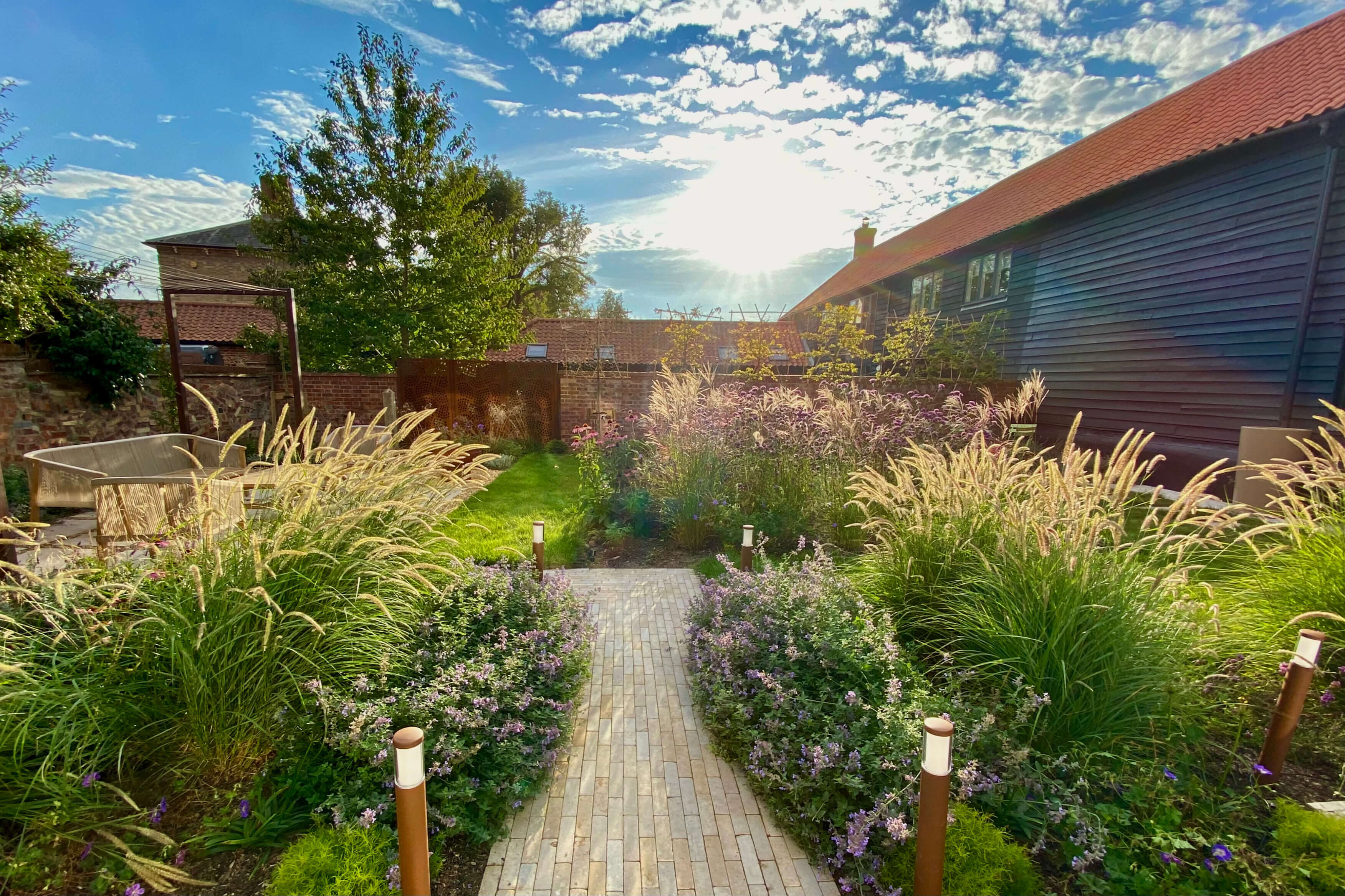 alt=”Contemporary Mediterranean-style garden in Suffolk by Rebecca Wallman Garden Design, with a central paver path, drought-tolerant grasses, and soft flowering plants.”