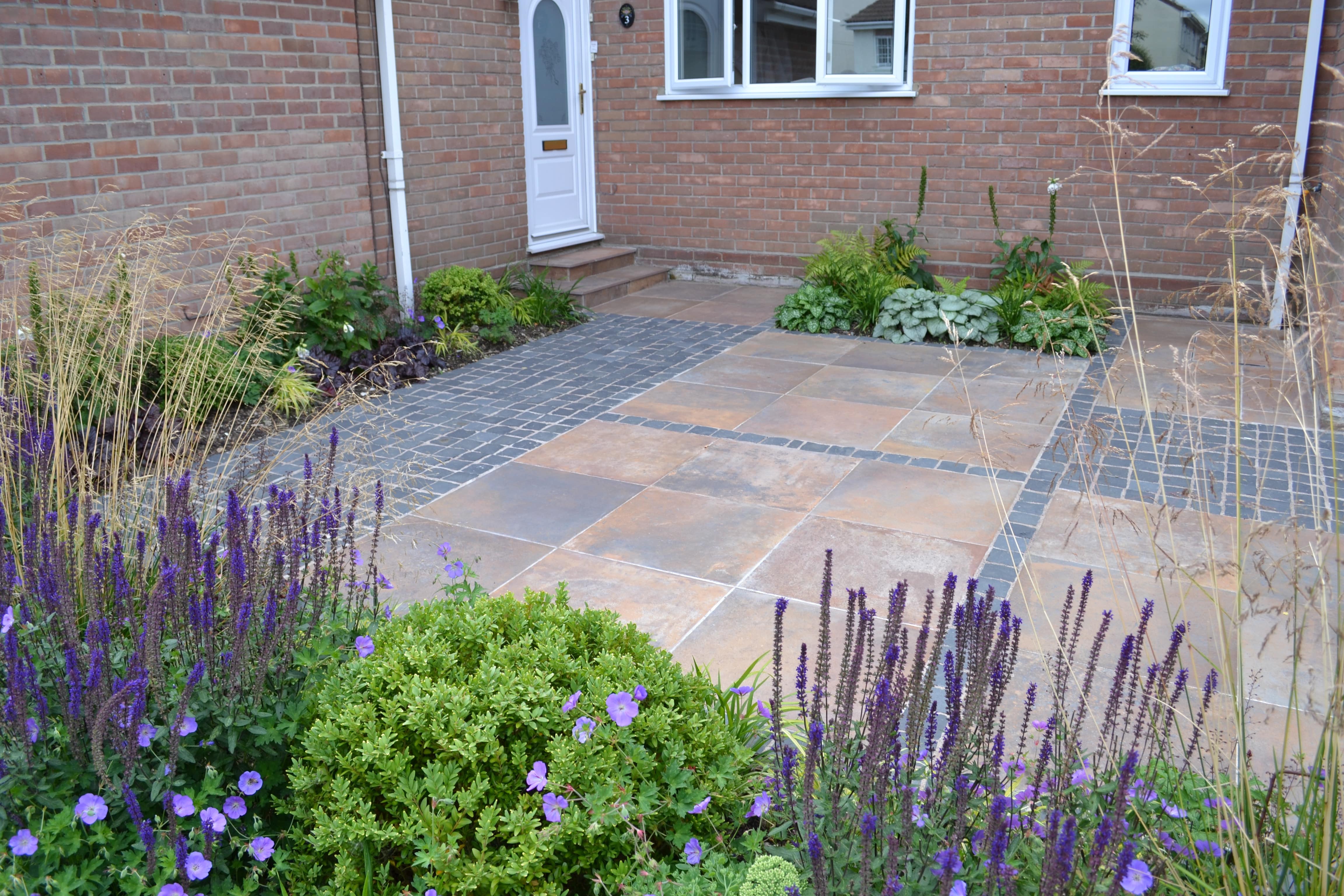 alt=”A contemporary front garden with porcelain paving, basalt setts and a purple planting scheme.”